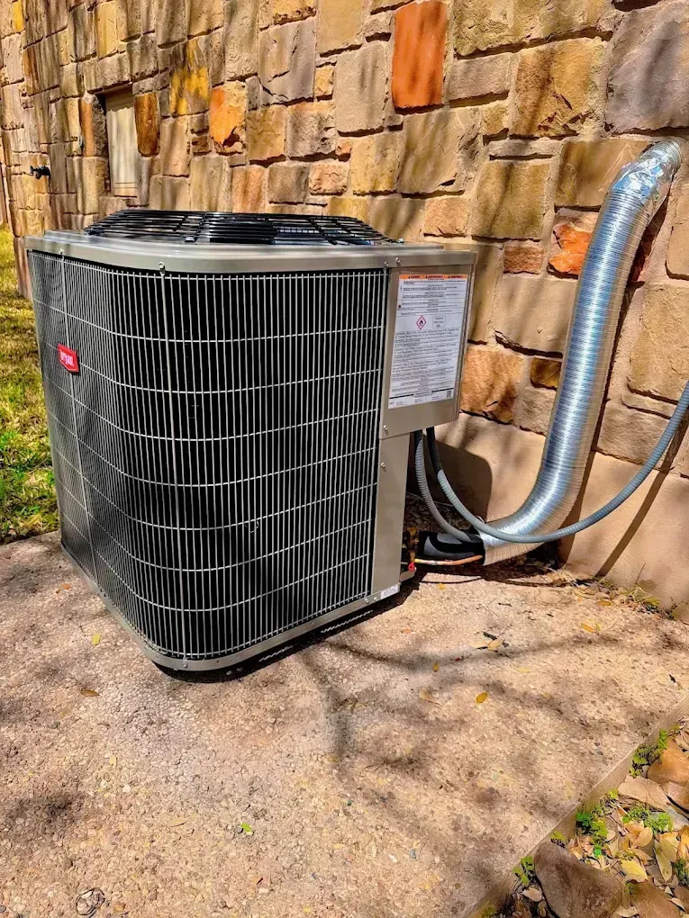 Outdoor air conditioner unit beside a stone wall, with insulated refrigerant lines attached.