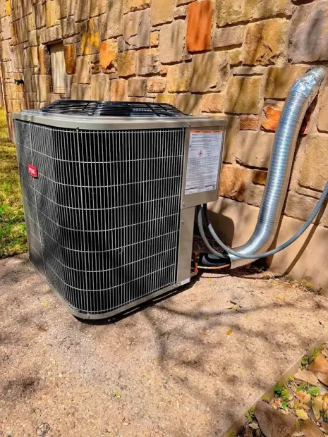 Outdoor central air conditioning unit beside a stone wall with insulated refrigerant lines attached