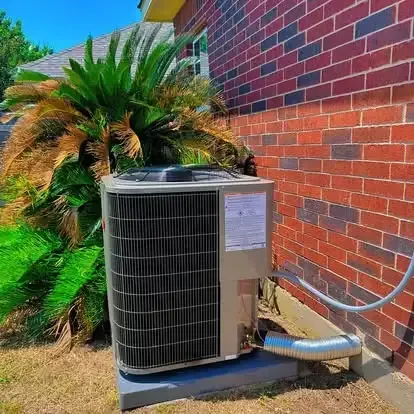 Outdoor air conditioner unit beside a red brick wall and palm plant
