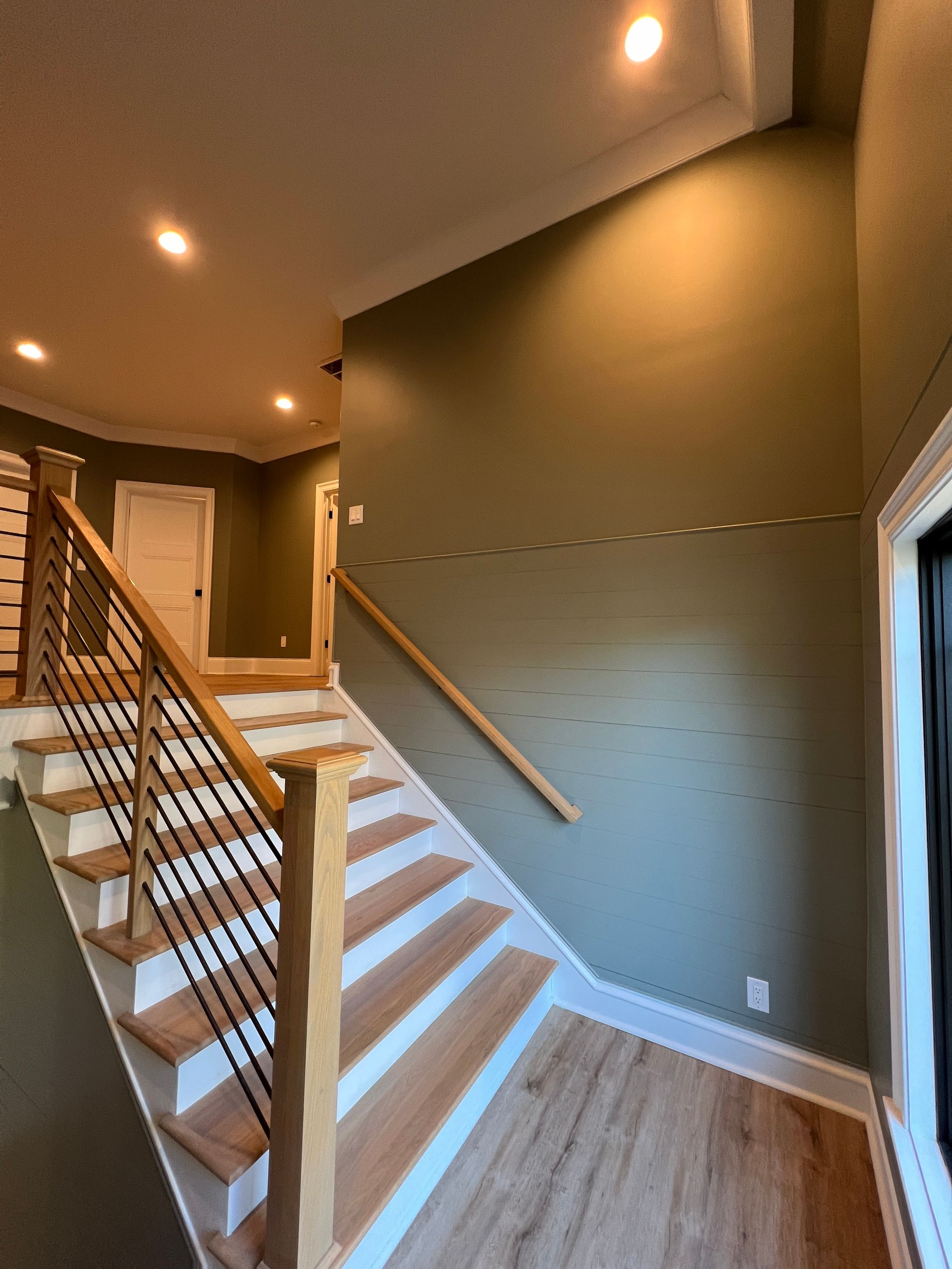 Staircase and hallway interior with wood steps, gray walls, and recessed ceiling lights