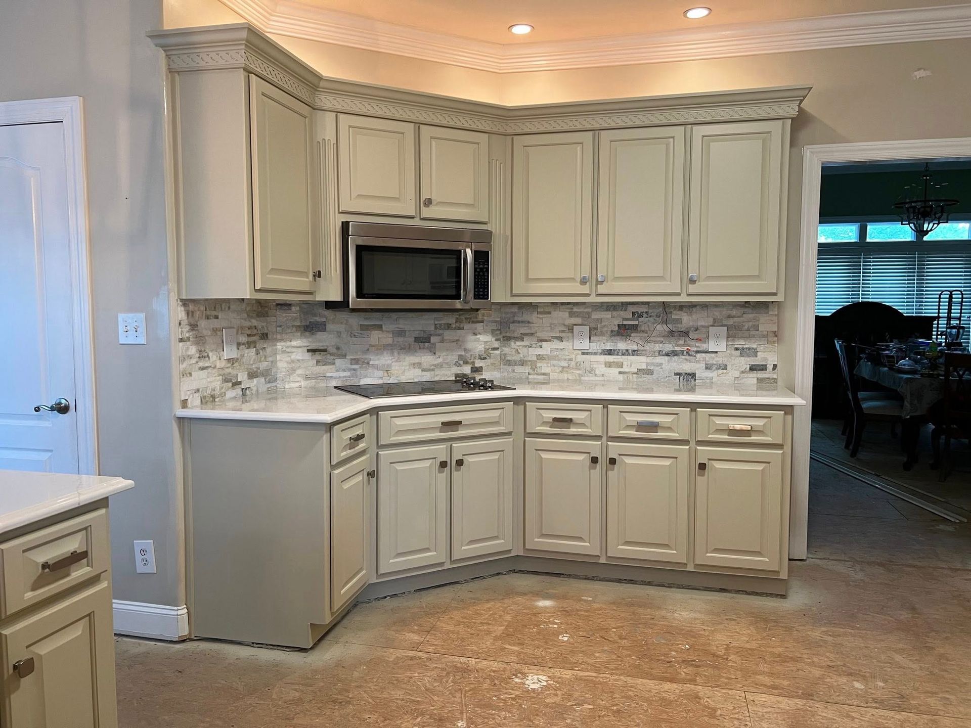 Beige kitchen with cream cabinets, mosaic backsplash, and built-in microwave and oven.