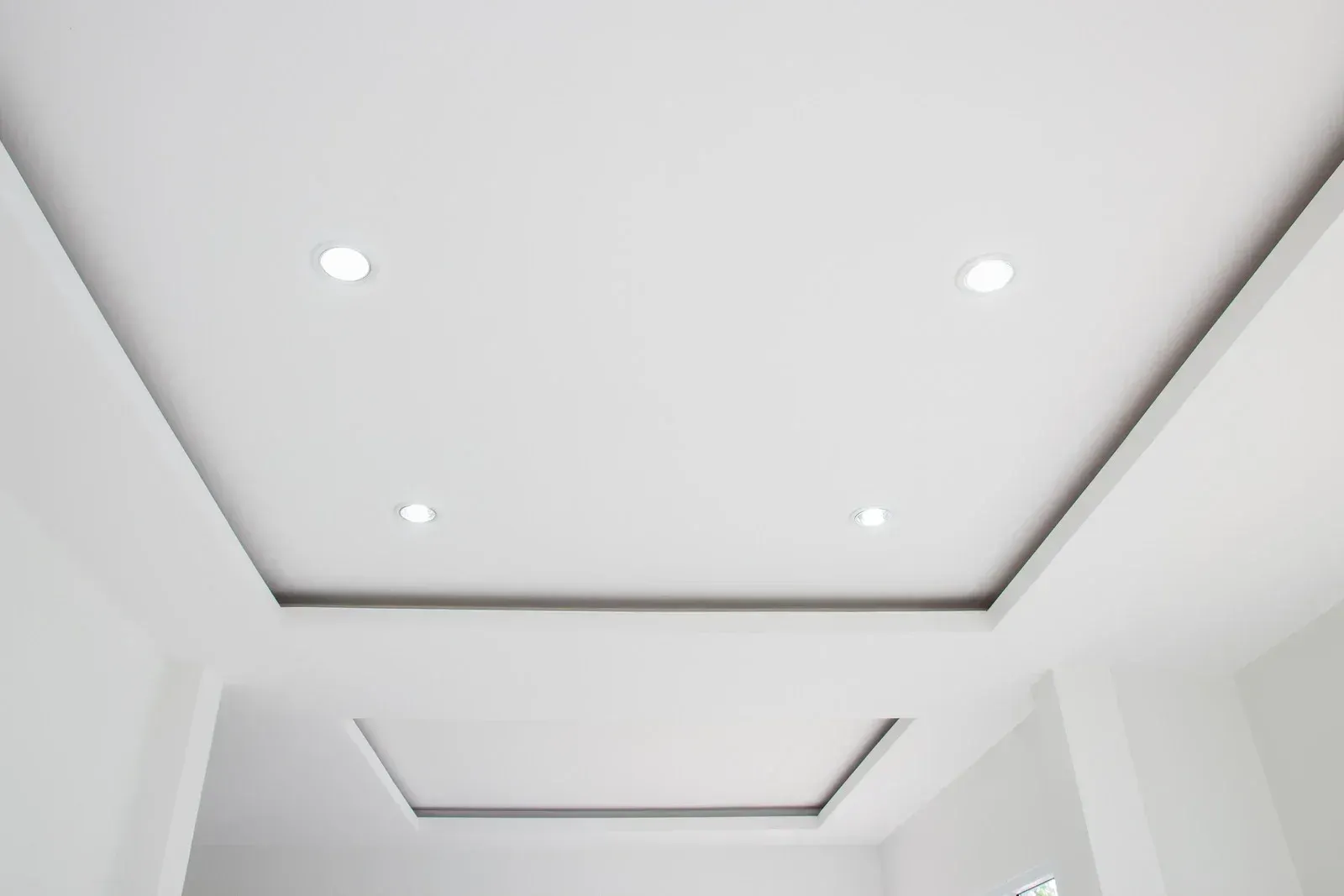White hallway ceiling with recessed lights and tray molding