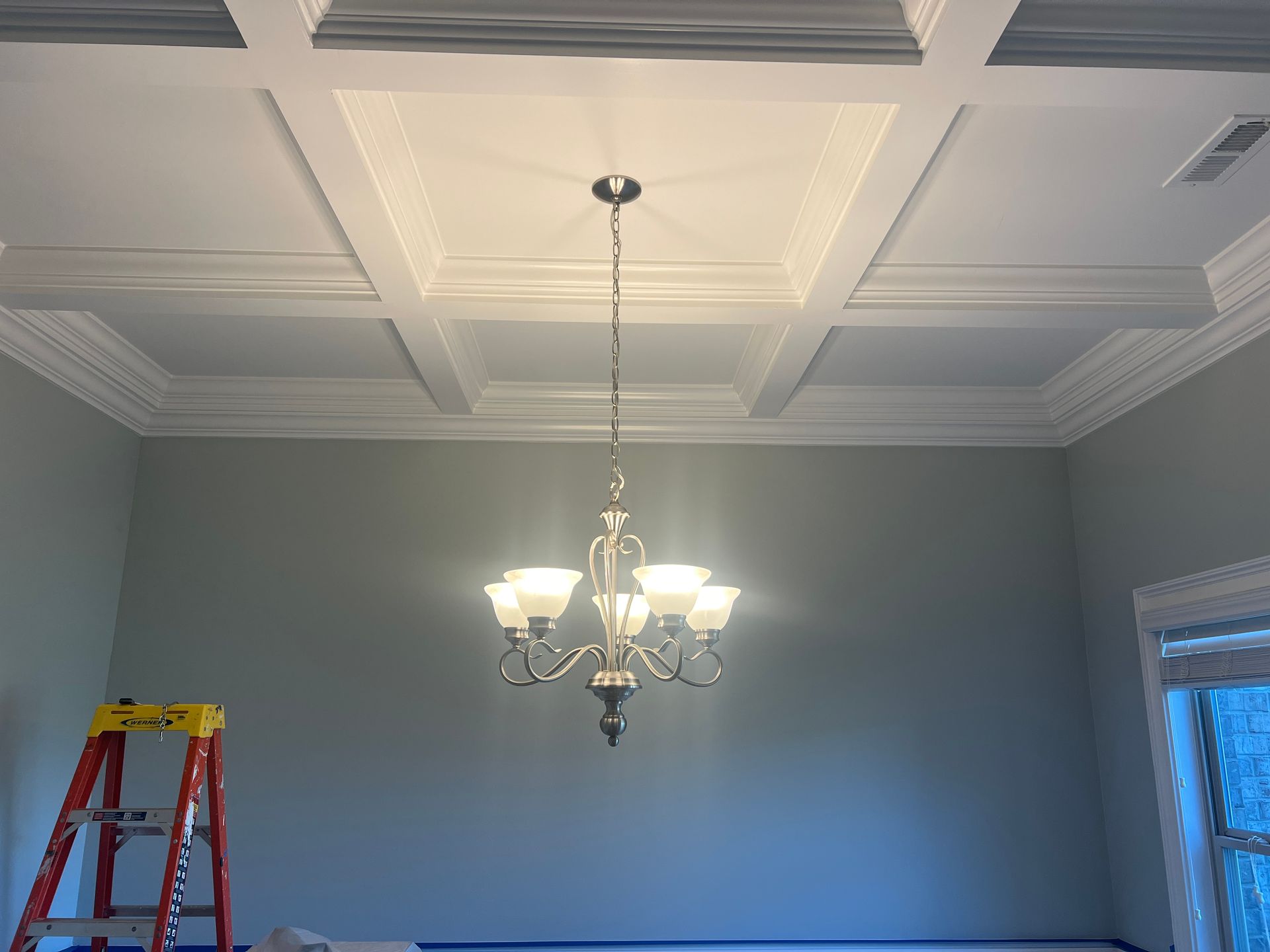 Dining room ceiling with recessed panels, a hanging chandelier, blue walls, and a red ladder at left.