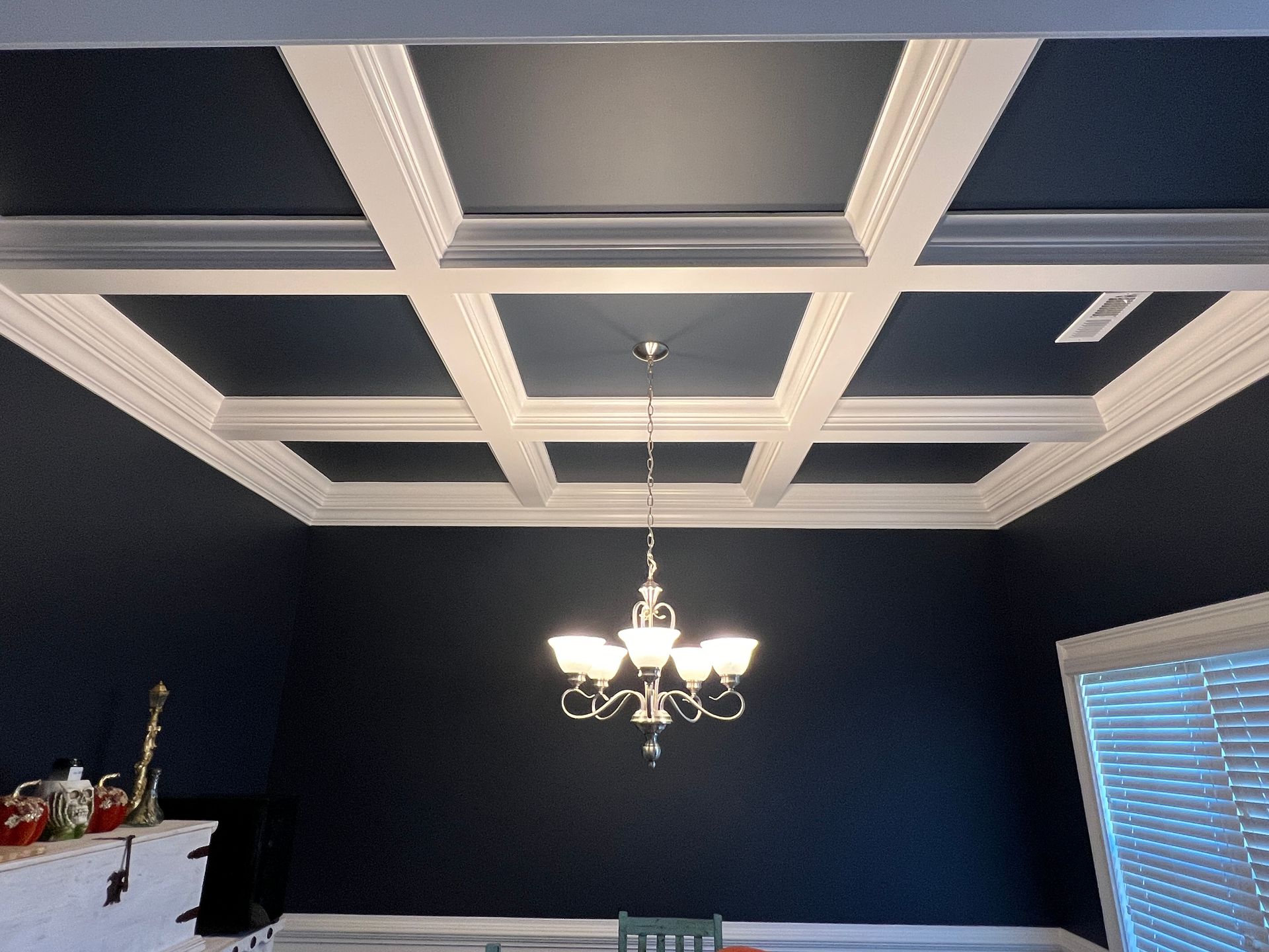 Coffered ceiling with dark navy walls and a hanging chandelier in a room