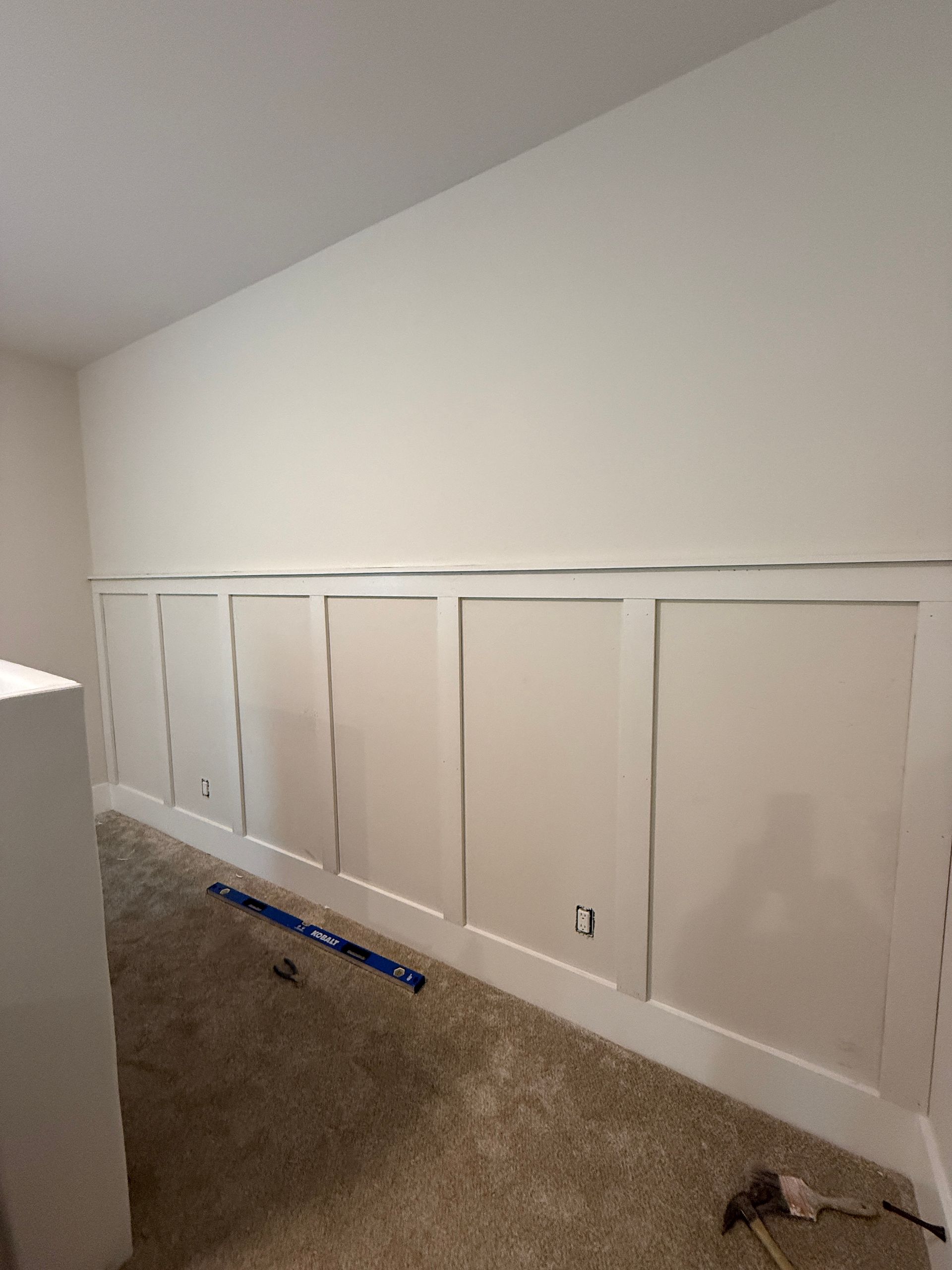 Empty carpeted room with white paneled wall trim and a high sloped ceiling
