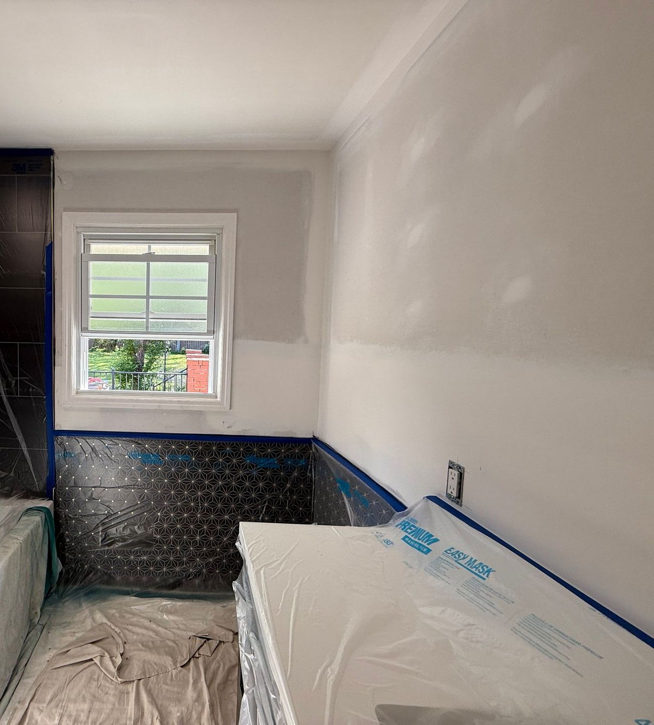 Freshly painted bathroom under renovation with white walls, black tile, and covered fixtures.