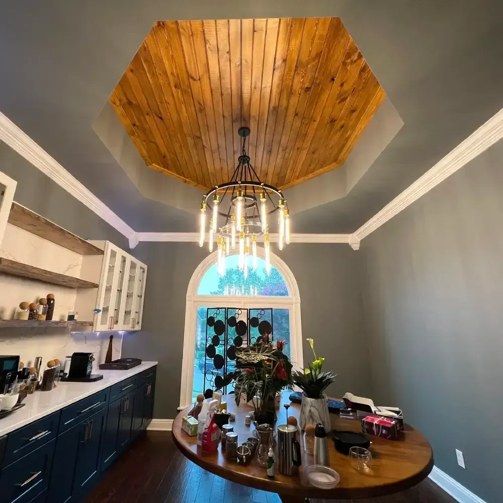 Dining room with gray walls, dark cabinets, round table, and a wood-paneled tray ceiling with chandelier.