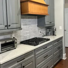 Modern kitchen with gray cabinets, white countertops, gas cooktop, and wood range hood