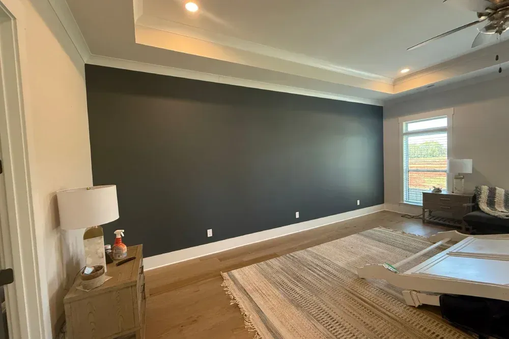 Modern living room with a dark accent wall, beige rug, and large windows.
