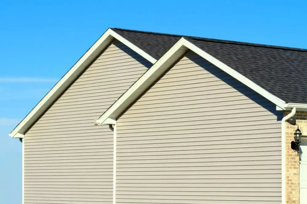 Suburban house exterior with beige siding and dark gray roof against a blue sky