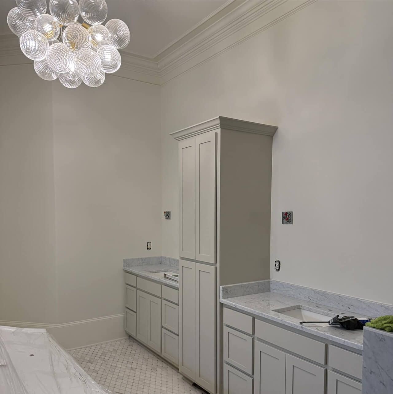 Bright white kitchen under construction with cabinets, marble-look counters, and a modern chandelier