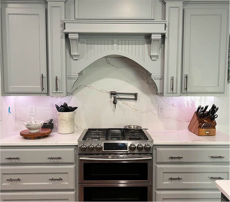 White kitchen with stainless steel stove, marble backsplash, and gray cabinets.