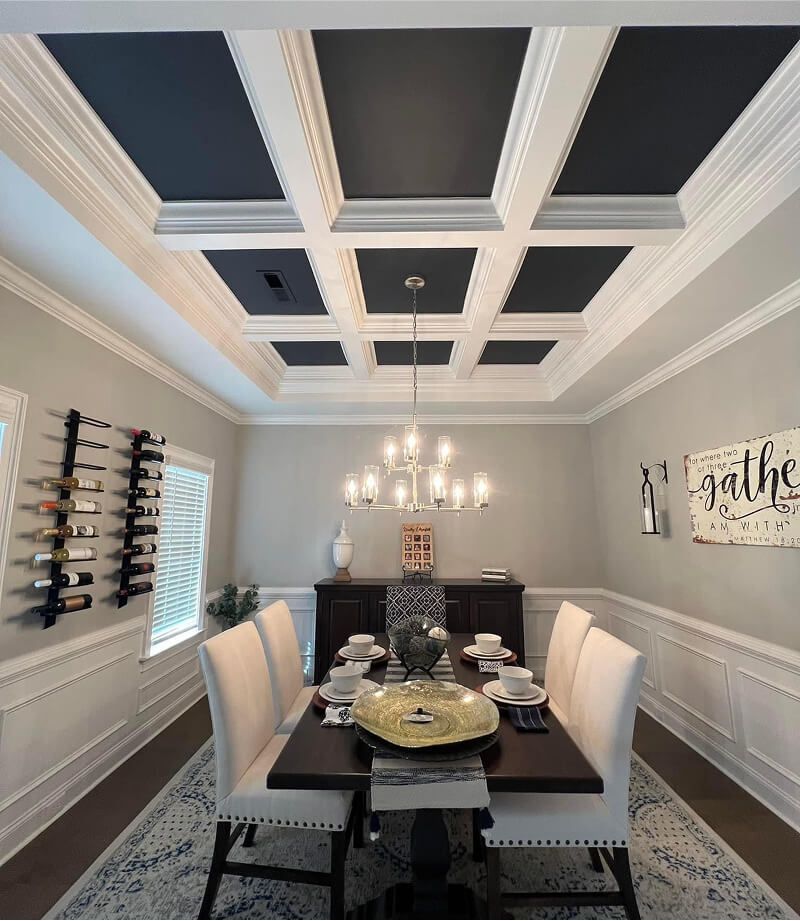 Formal dining room with black ceiling panels, white walls, chandelier, and a dark wood table with upholstered chairs