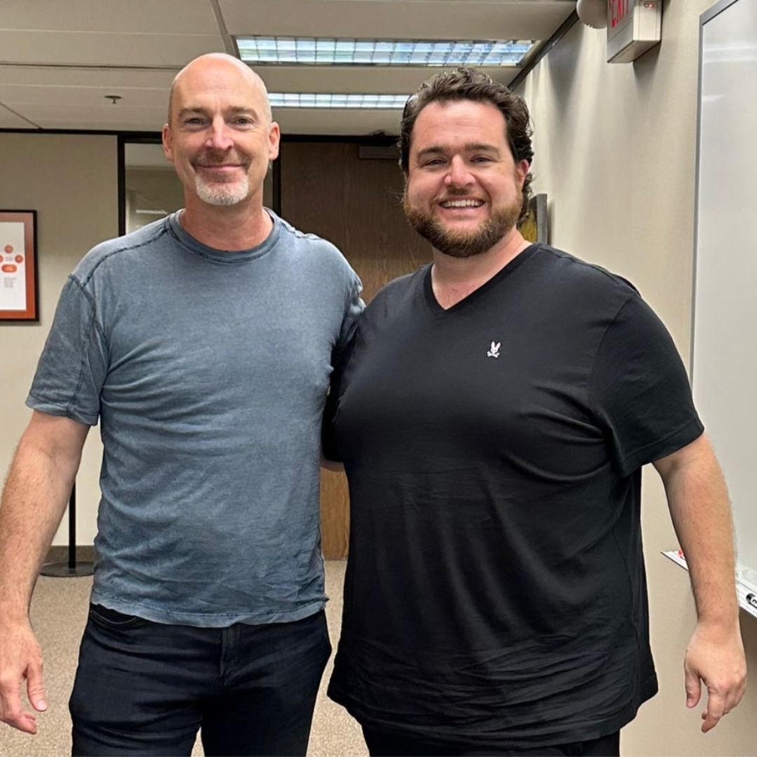 Two men are posing for a picture together in a hallway.