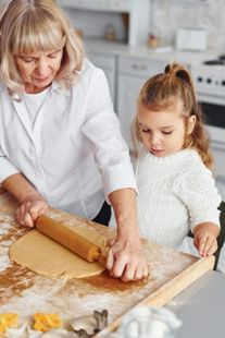 Older woman and child rolling dough on a floured table in a bright kitchen
