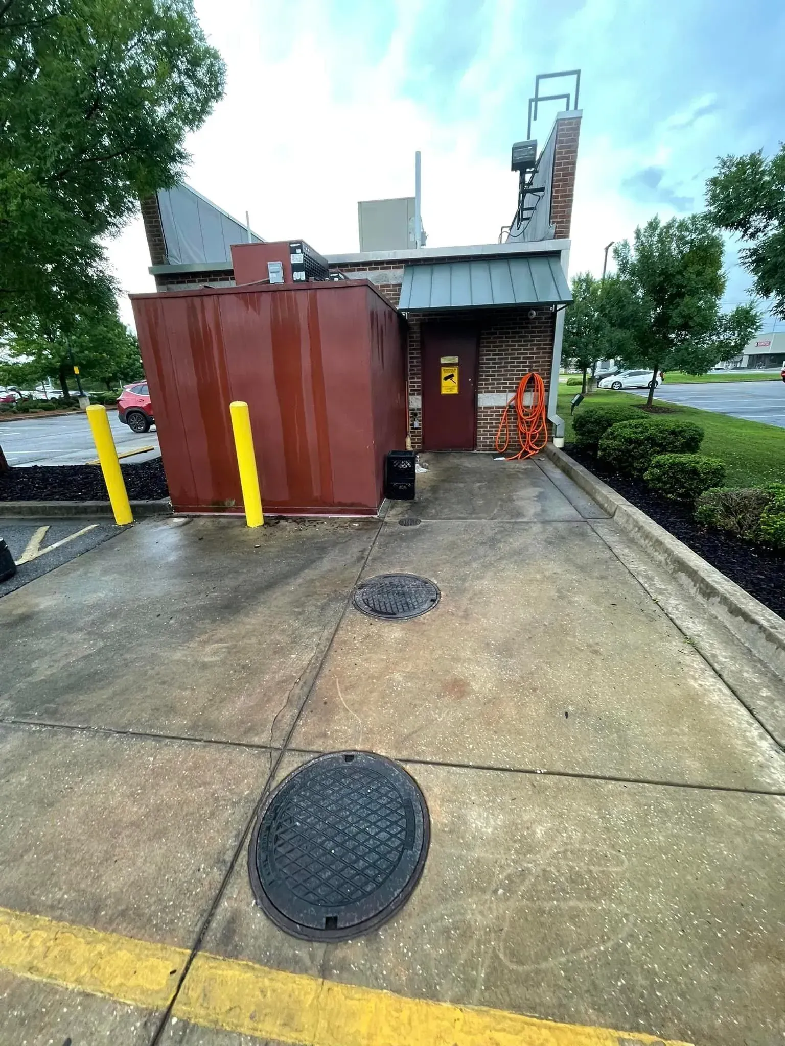 Exterior of a building with a large brown dumpster, yellow posts, and gray concrete ground.