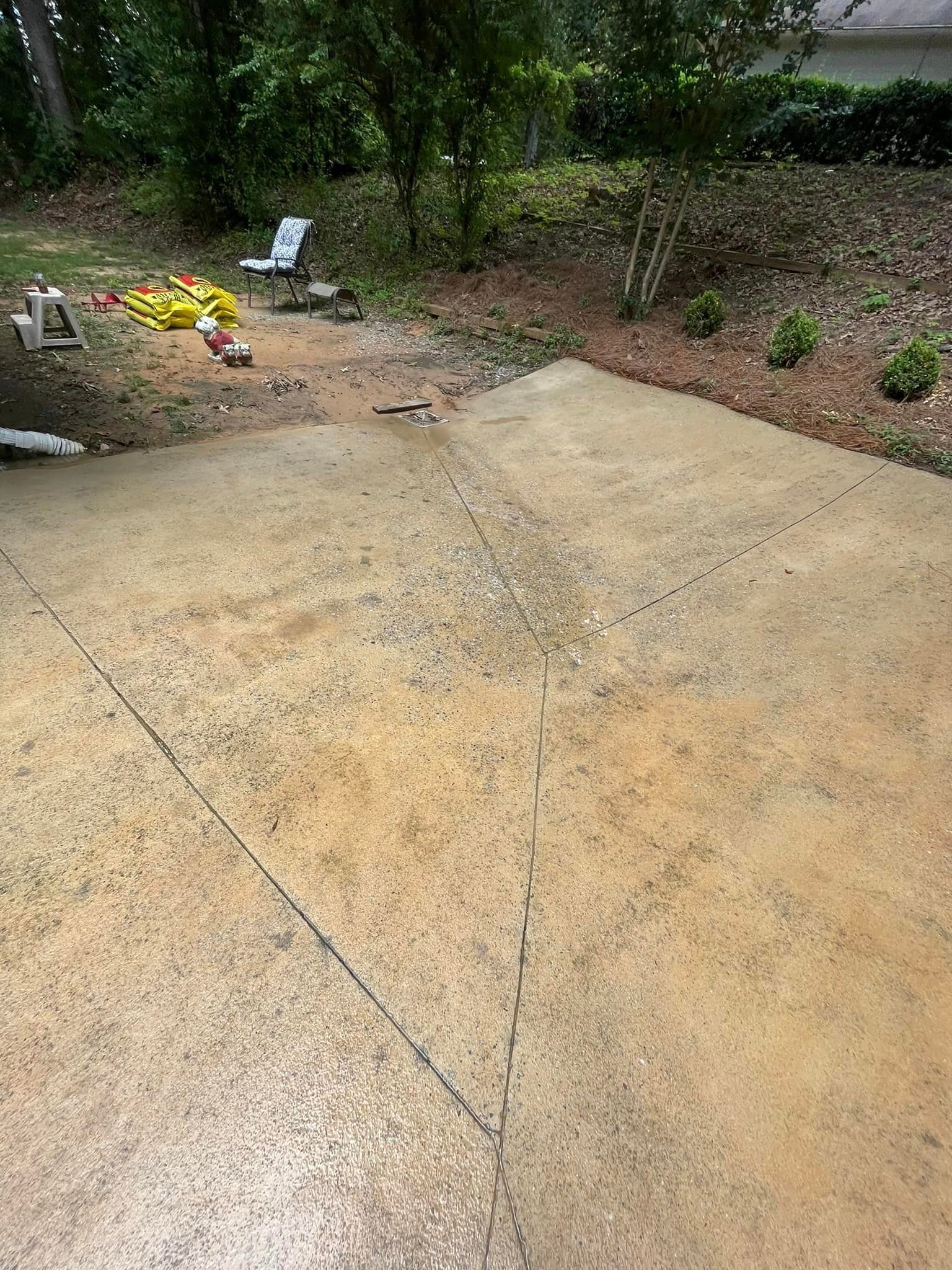 Concrete patio in a yard with a garden bed and trees in the background.