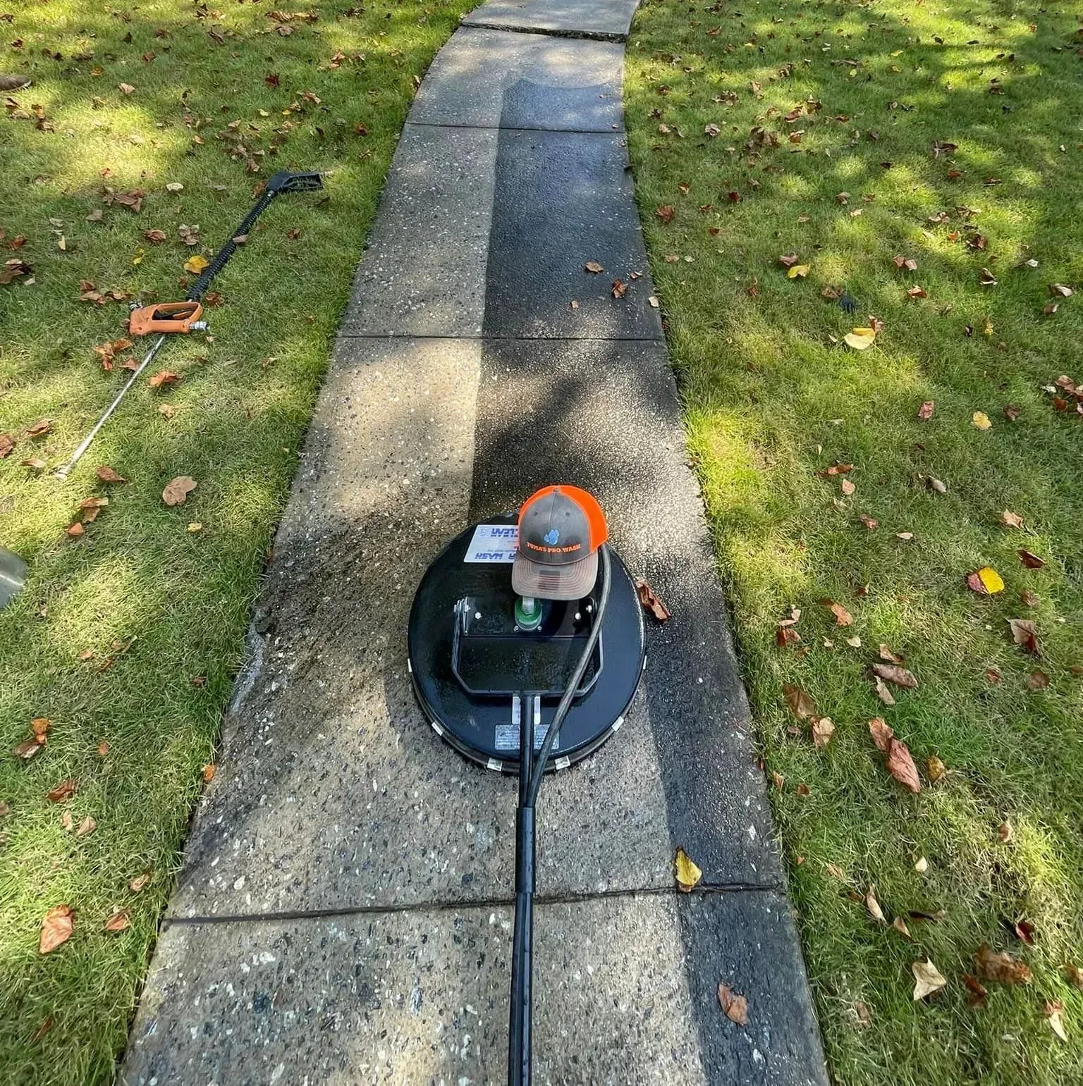 Man using a circular surface cleaner to power wash a stone walkway.