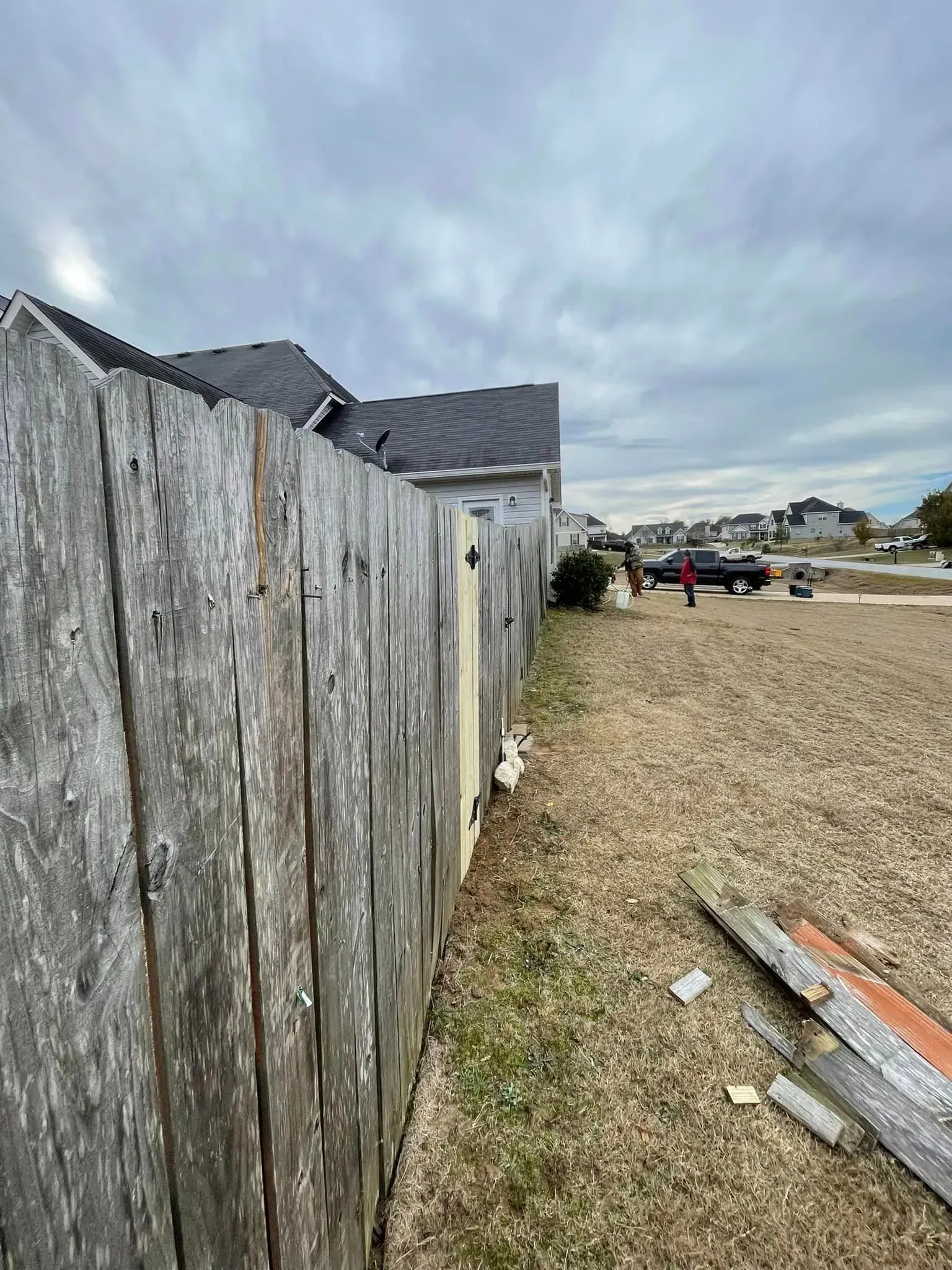 Weathered wooden fence with a house in the background and a cloudy sky.