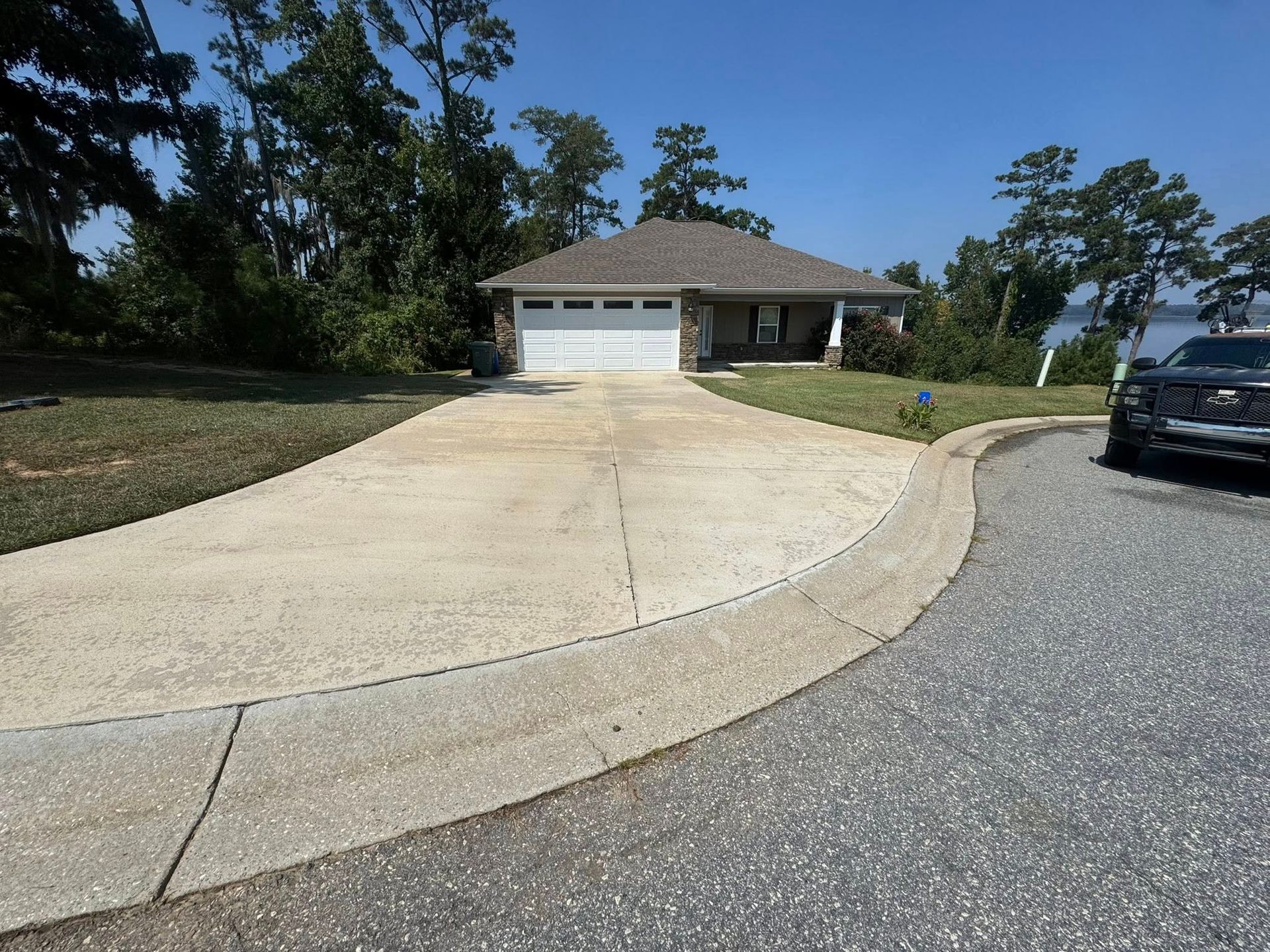 House with gray roof and white garage door, concrete driveway curves into street, blue sky.
