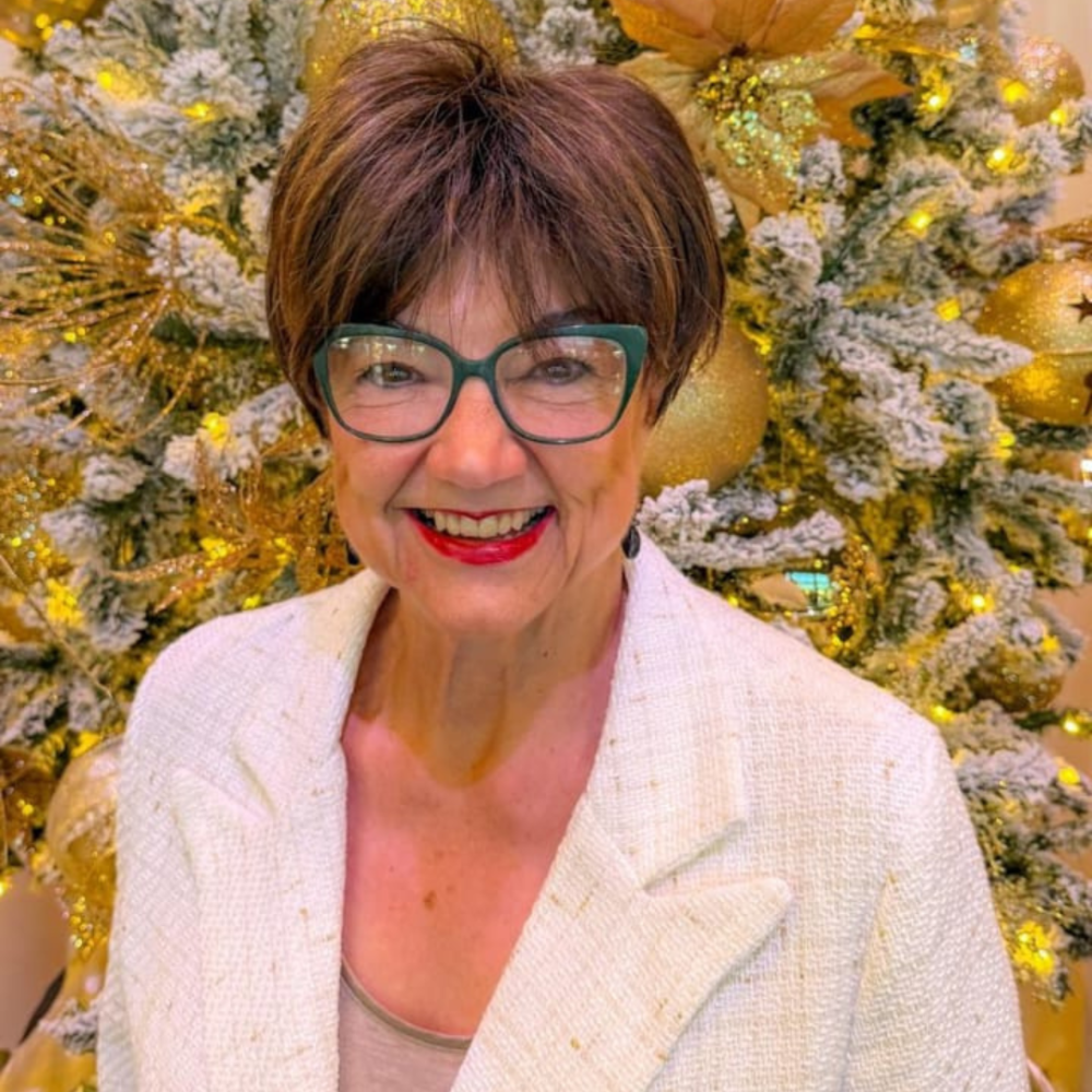 Smiling woman with glasses in front of a gold-and-white holiday tree