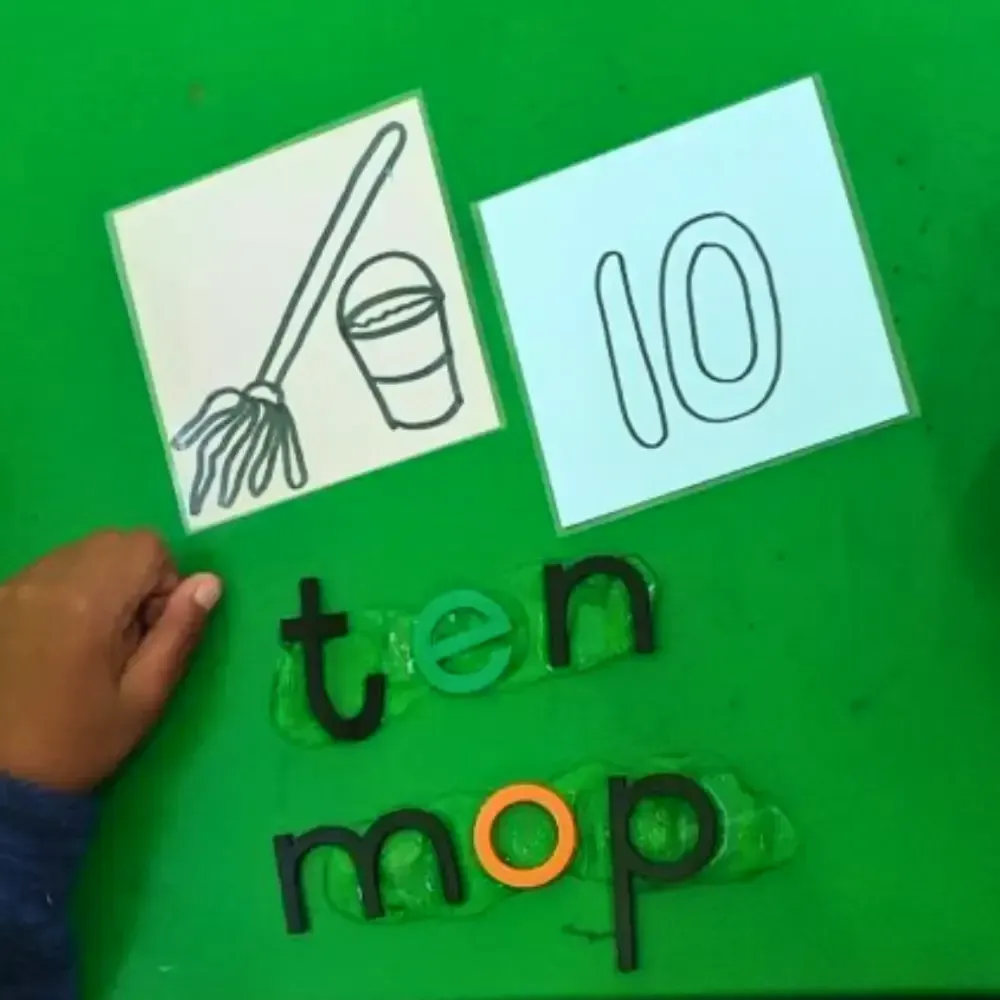 Child's hand near cards showing a mop, bucket, the number 10, and the word 