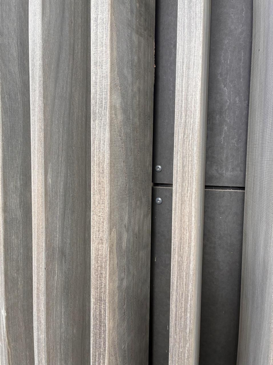 Close-up of gray wooden fence slats with narrow vertical gaps and visible screws