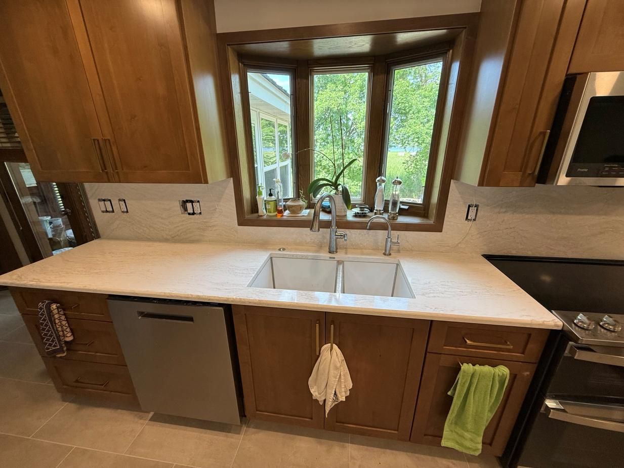 Wooden kitchen with white countertops, double sink, and window overlooking greenery.
