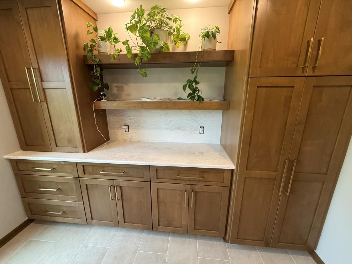 Built-in wooden cabinets and countertop with open shelves and potted plants in a laundry room