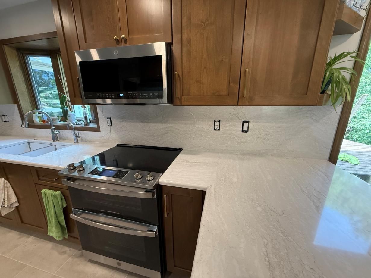 Modern kitchen with wood cabinets, white countertops, stainless stove, and built-in microwave near a sink and window.