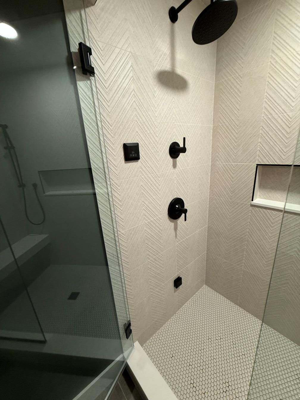 Modern glass shower with white textured tile, black fixtures, and a shower head against the wall