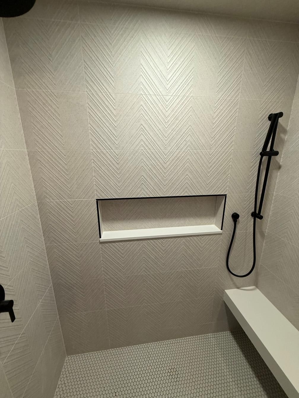 Small tiled shower with a recessed shelf, handheld showerhead, and built-in bench.