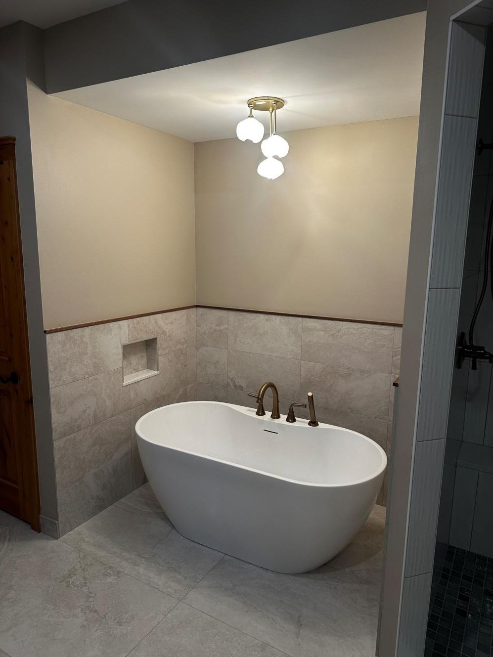 Small bathroom with a freestanding oval tub, beige walls, gray tile, and a ceiling light fixture.