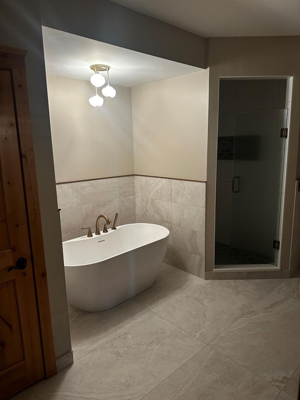 Modern bathroom with freestanding tub, beige tile walls, and glass shower enclosure