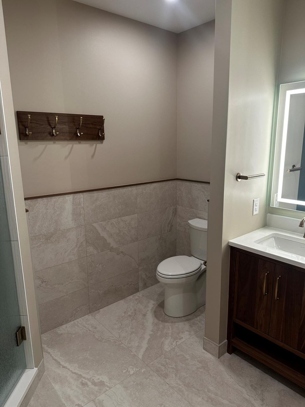 Small bathroom with toilet, wall hooks, vanity sink, and mirror in neutral tones