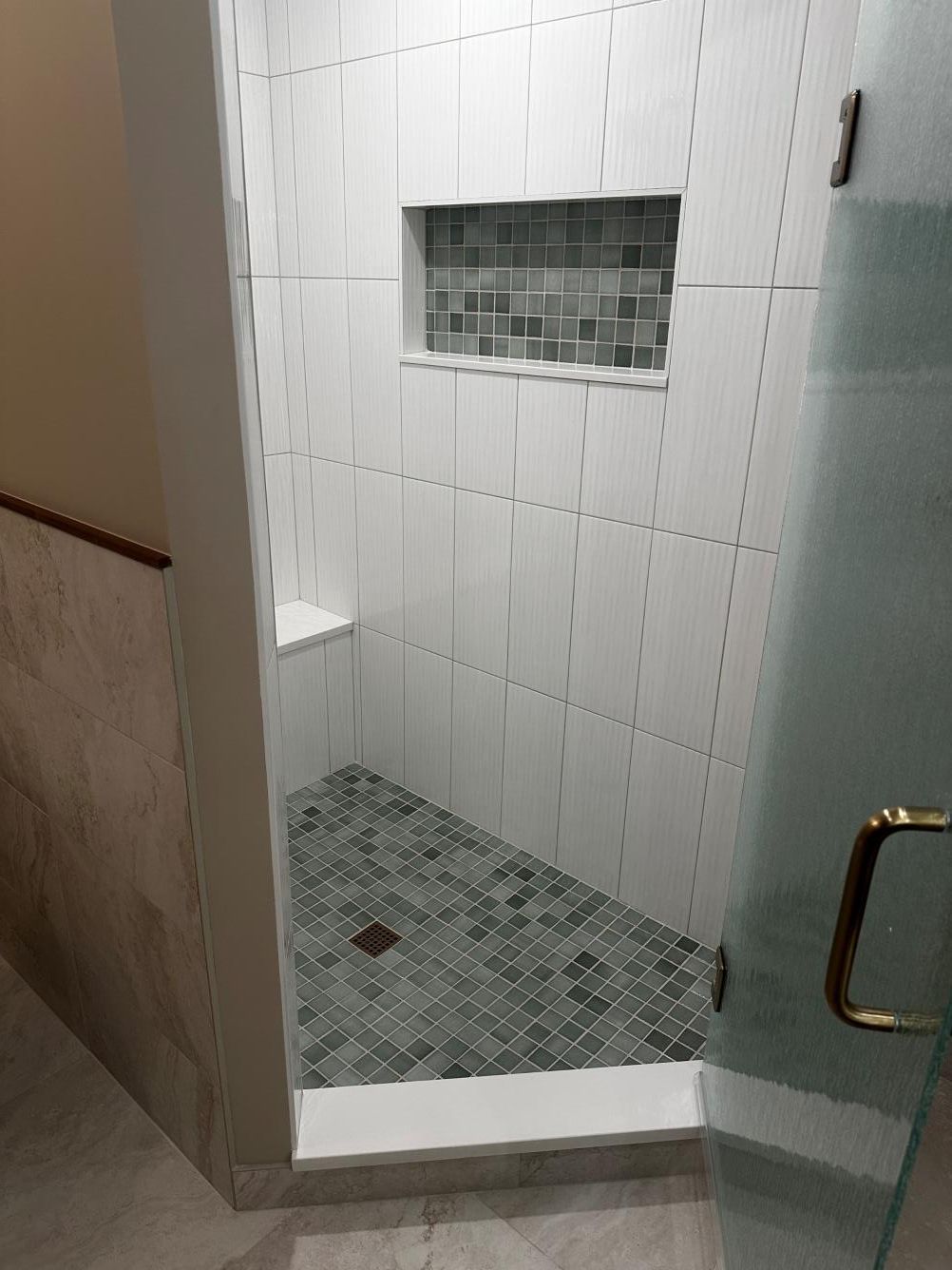 Small tiled shower stall with a low step, mosaic floor, and frosted glass door