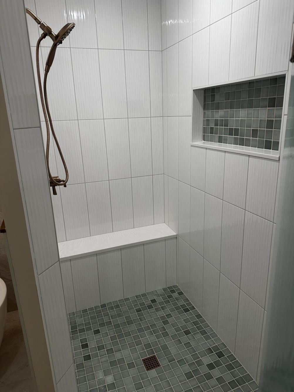 White tiled shower with a built-in bench, dark mosaic floor, and small recessed shelf.
