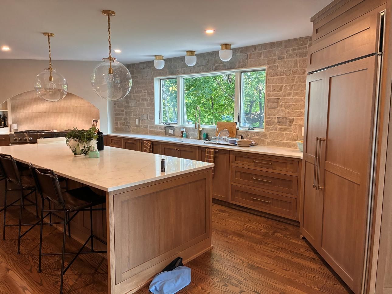 Bright kitchen with island, pendant lights, wood cabinets, and brick wall by a window