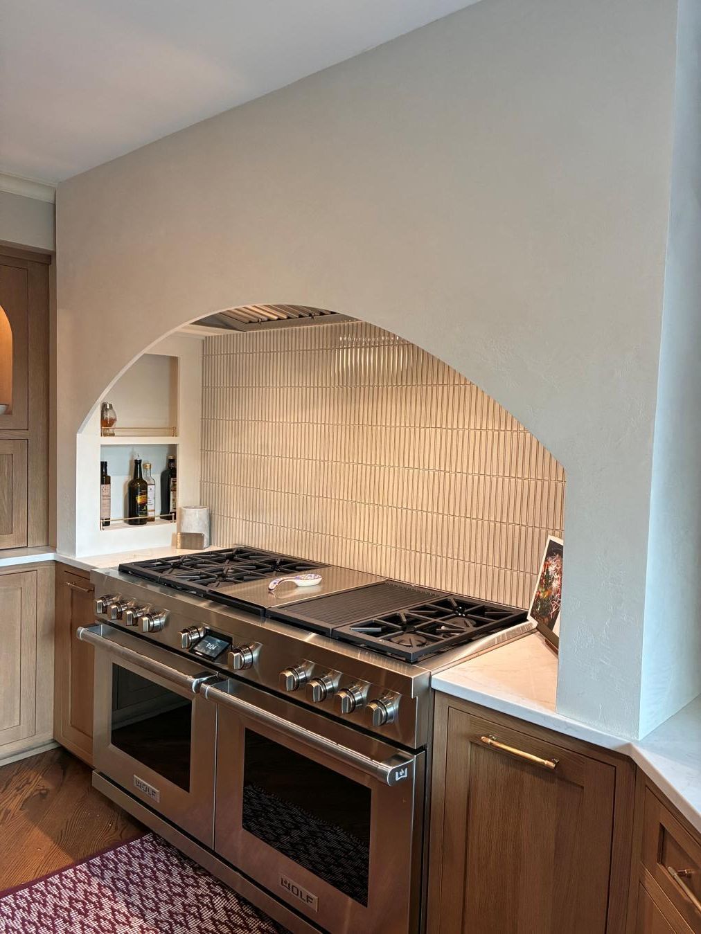 Modern kitchen with stainless steel double oven, gas cooktop, and arched pass-through opening