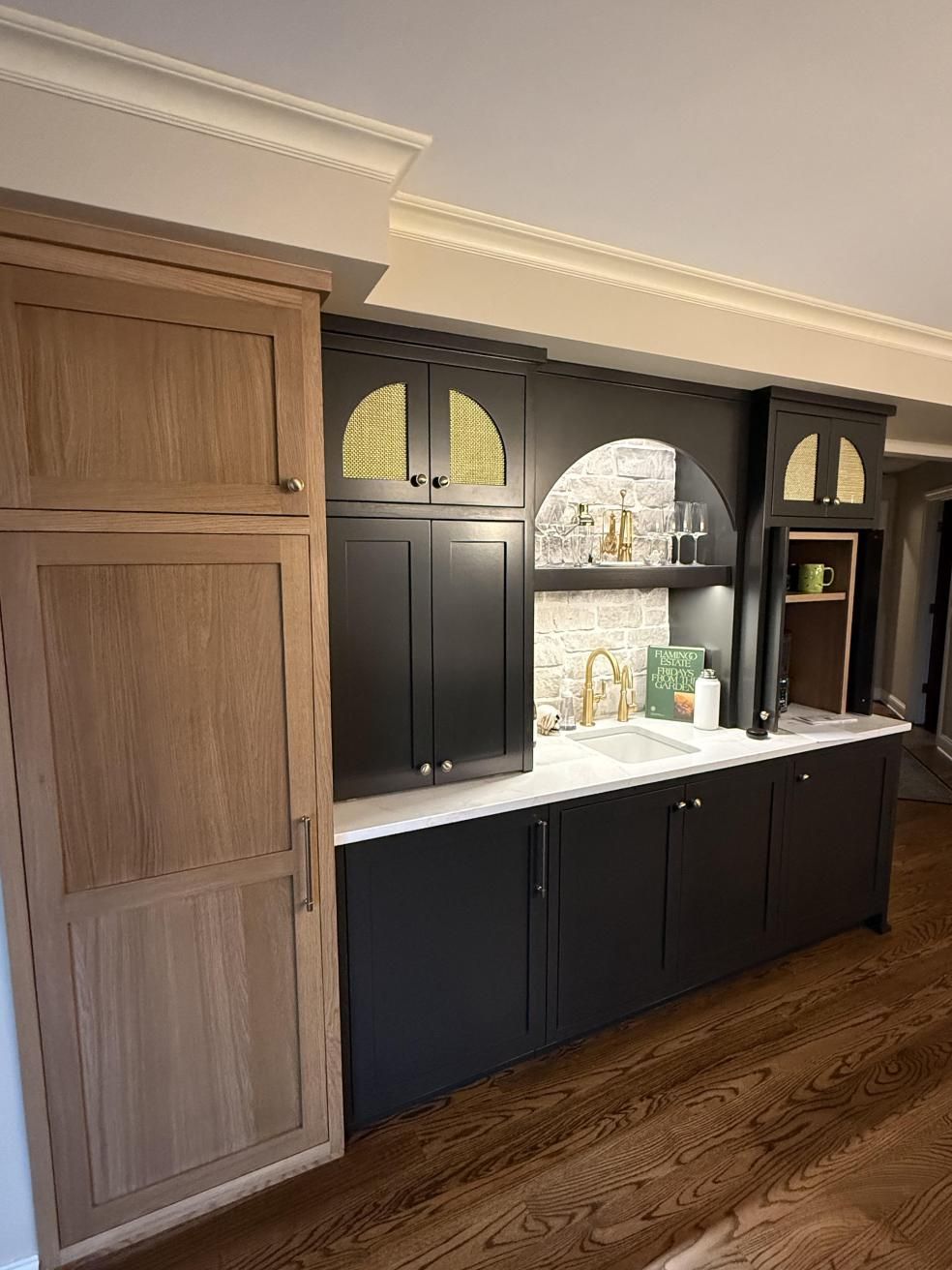 Built-in dark cabinets with white countertop, arched niches, and tall wood pantry in a kitchen.