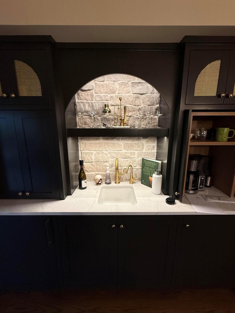 Built-in black cabinets framing a white sink and arched stone backsplash in a modern kitchen niche