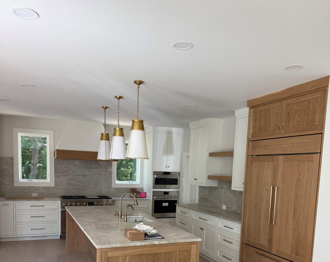 Bright modern kitchen with white cabinets, marble island, gold pendant lights, and built-in wood refrigerator panel.