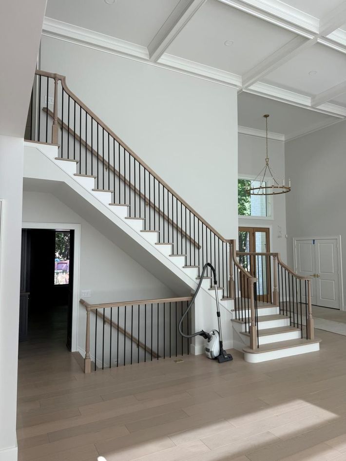 Spiral staircase with black railing in a sunlit room with hardwood floors and a tall window