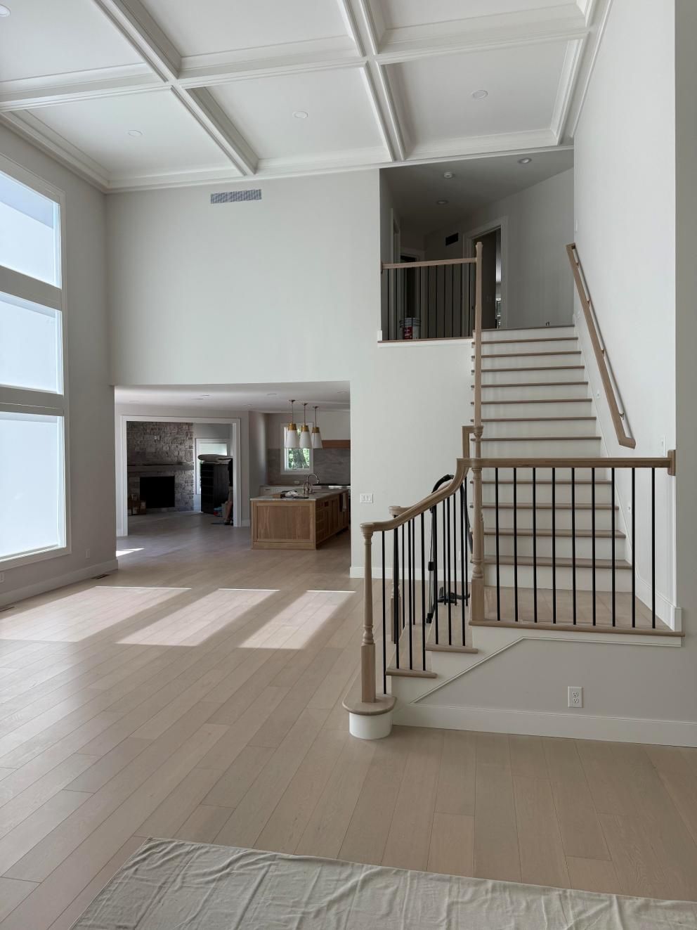Bright open living room with staircase, white walls, and sunlight on light wood floors