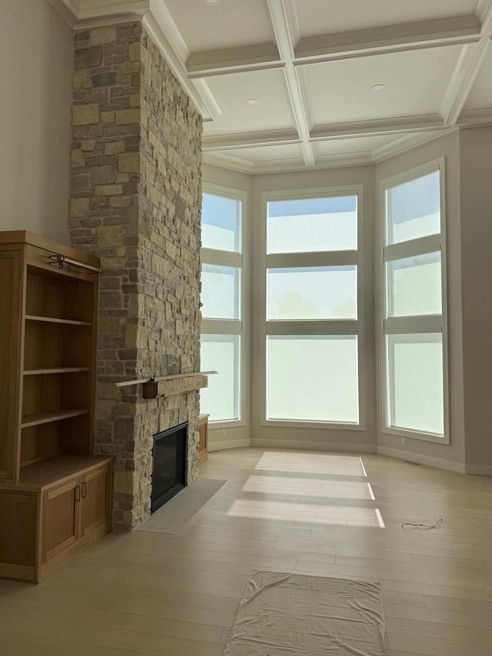 Bright empty living room with stone fireplace, built-in shelves, and large bay windows.