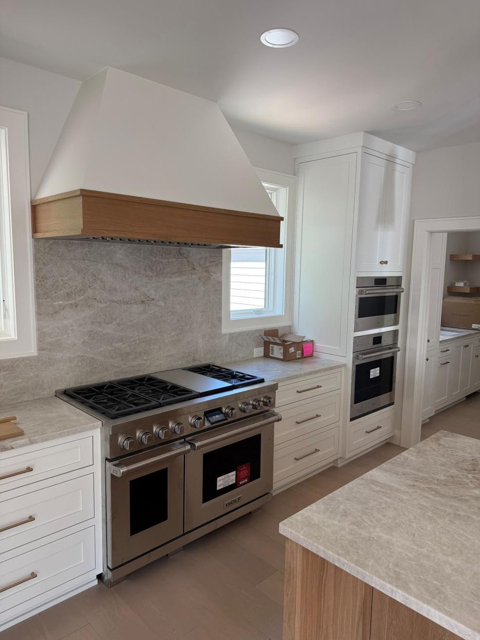 Modern white kitchen with stainless steel stove, beige countertops, and built-in oven cabinets