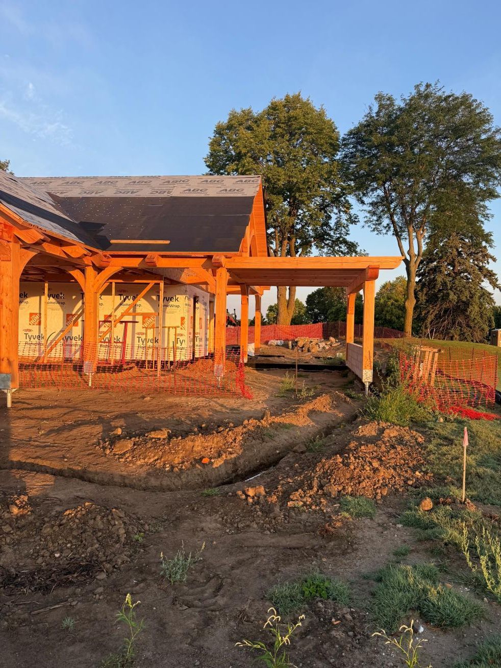 Orange house under construction with wooden porch framing and muddy yard in warm evening light