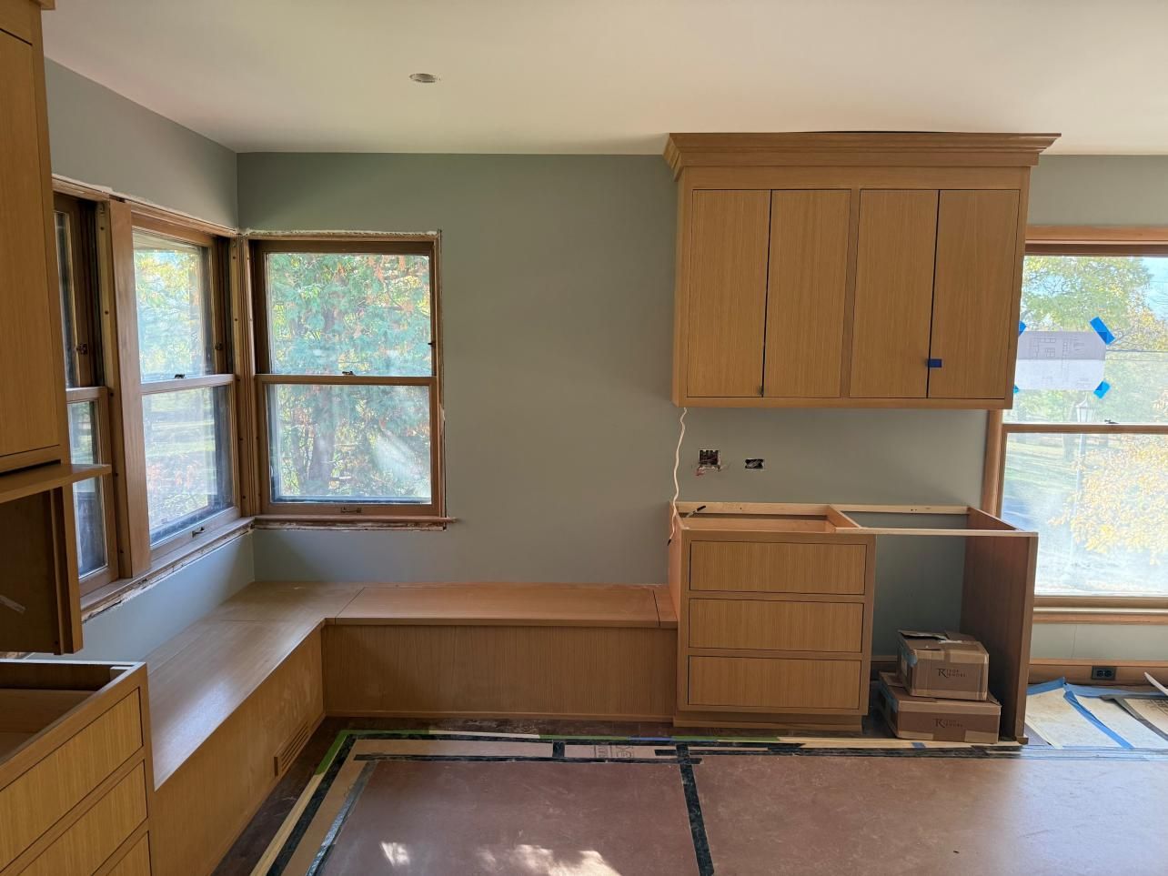 Empty kitchen with light wood cabinets, corner bench seating, and large windows.