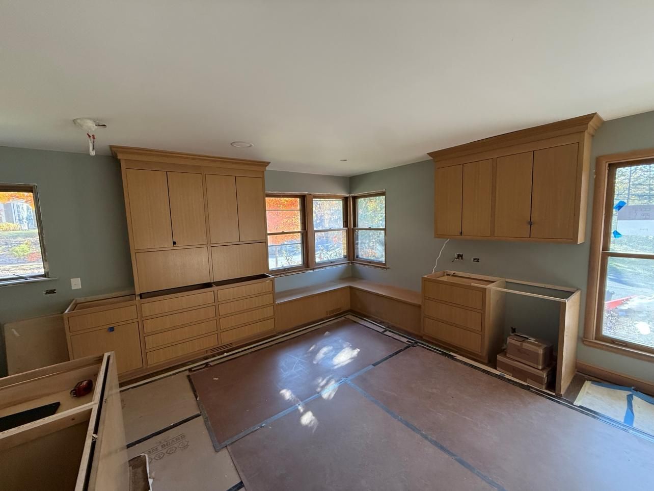 Unfurnished room with built-in wooden cabinets, gray walls, and windows letting in sunlight.
