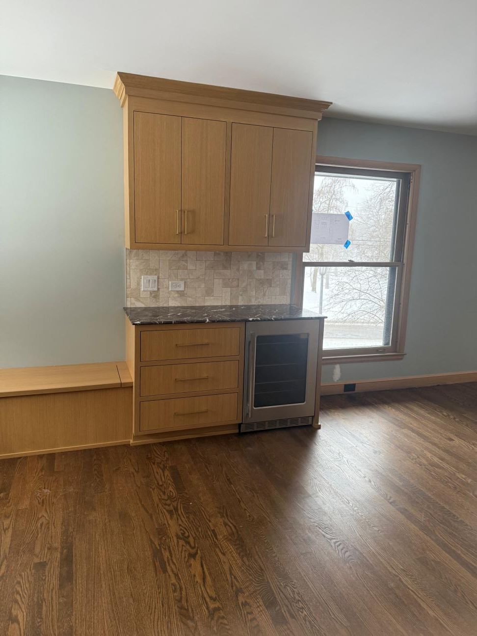 Built-in wooden cabinets and drawers beside a window in an empty room with wood flooring